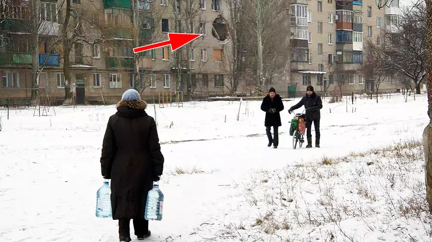 Авдеевка - женщина несет воду на фоне разбитой украинским снарядом пятиэтажки.